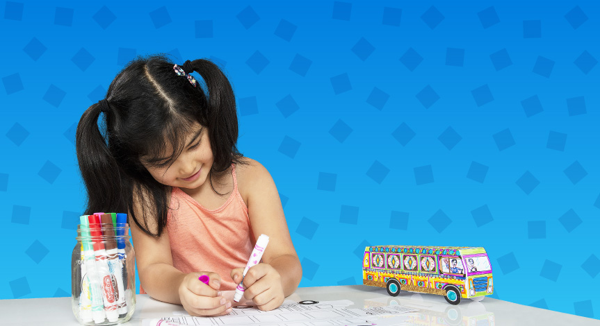 Girl coloring a Crayola Imagine Arts Academy bus take home while a completed version is next to her on the table. Image is on